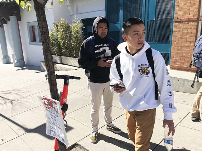 Senior Cole Slater and junior Trieu Tran wait for the school shuttle next to a Jump scooter parked in front of the Pine/Octavia campus. Electric scooter-sharing systems like Jump, Skip, Spin and Lime brought thousands of new scooter units to San Francisco after securing city permits in 2019, but the rise in scooters is correlated with a rise in injuries.