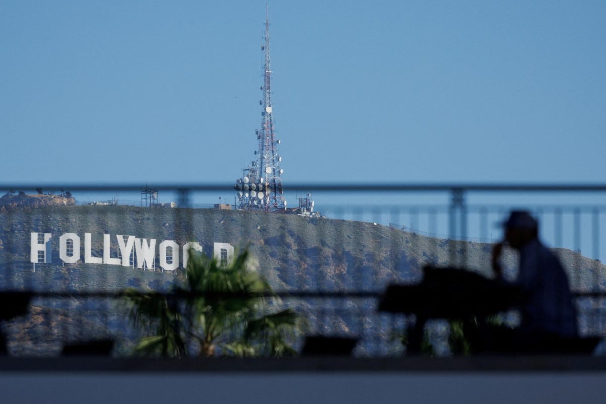 The iconic Hollywood sign is shown behind a person sitting in the shade along Hollywood Blvd as the city prepares to host the 97th Academy Awards in Los Angeles, California, U.S., February 25, 2025.